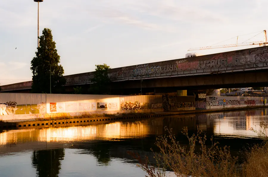 Le quai, au couchant — Le soleil rase le mur du quai et allume les graffitis. L'eau ne bouge pas.