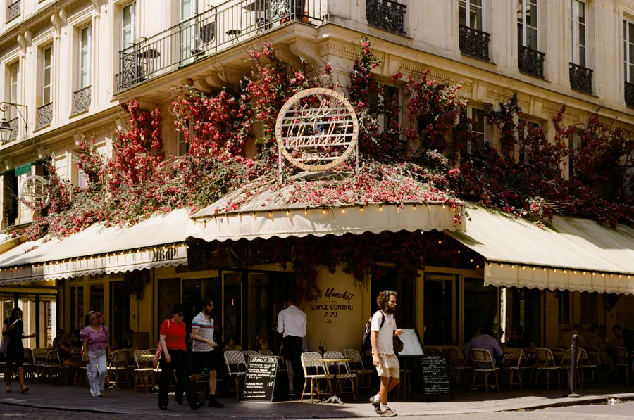 Le café fleuri — Un angle de rue entièrement recouvert de fleurs artificielles, et les serveurs q