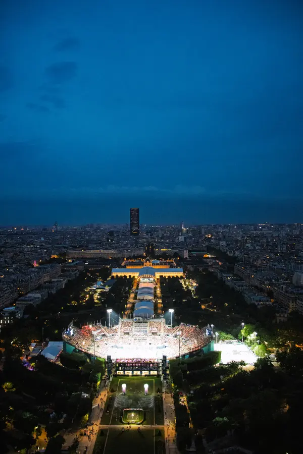 L'arène du Champ-de-Mars — Le stade provisoire posé dans le jardin, allumé à l'heure bleue, comme un objet 