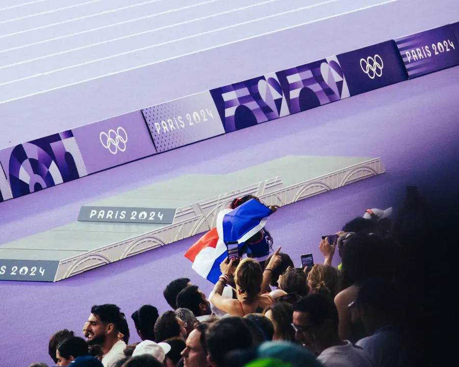 Le drapeau — Un drapeau tricolore passe de main en main au-dessus de la barrière, du côté du 