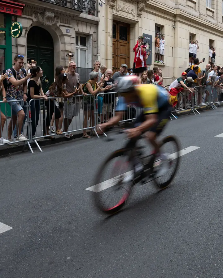 Le passage — Un coureur file entre les barrières, filé au 1/30e. Le public tient tout le cadr