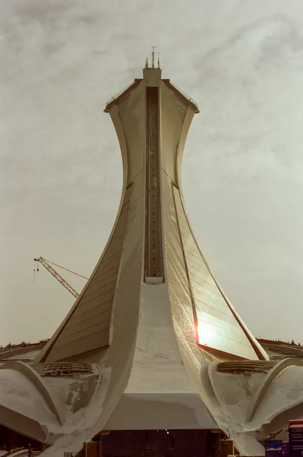 La tour — Le mât du Stade olympique, vu du pied, contre un ciel de neige. La courbe de bét