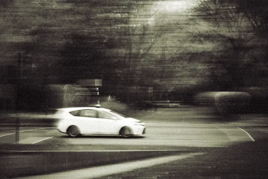 Filé — Une voiture blanche traverse le cadre à vitesse lente ; tout le reste s'étire av