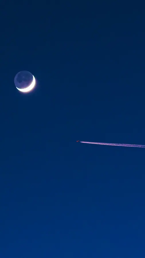 Lune et traînée — Un croissant de lune et la traînée d'un avion sur un bleu profond. Rien d'autre 